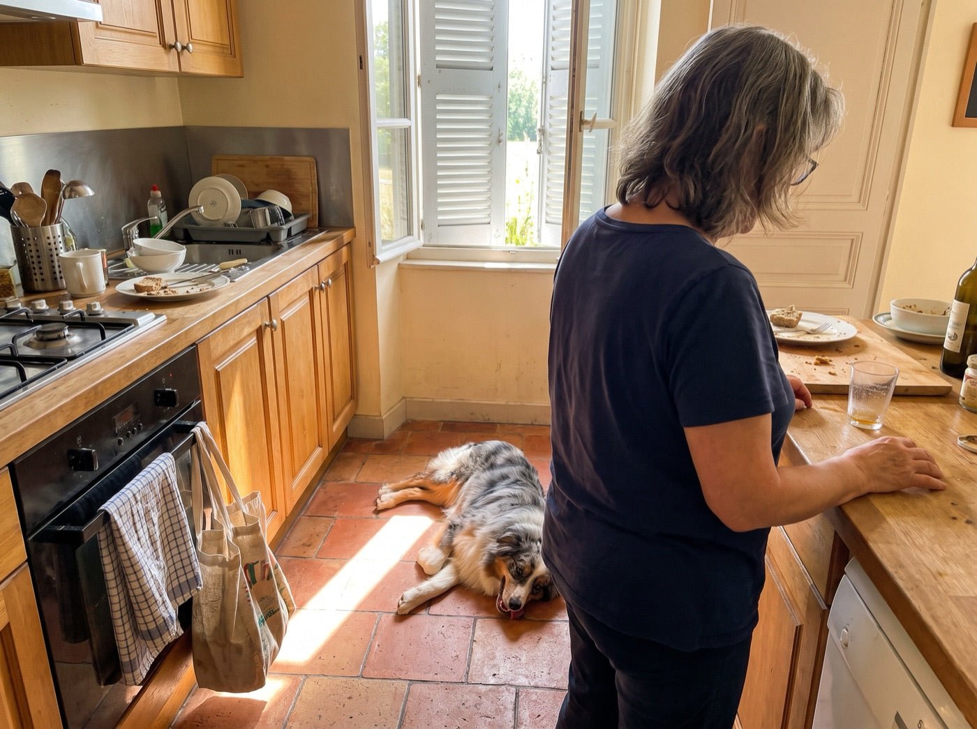 Une femme dans sa cuisine, son chien couché sur le carrelage derrière elle