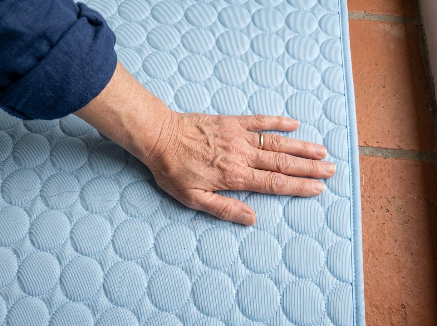 Une main de femme posée à plat sur le tapis rafraîchissant, à côté d'une tomette nue